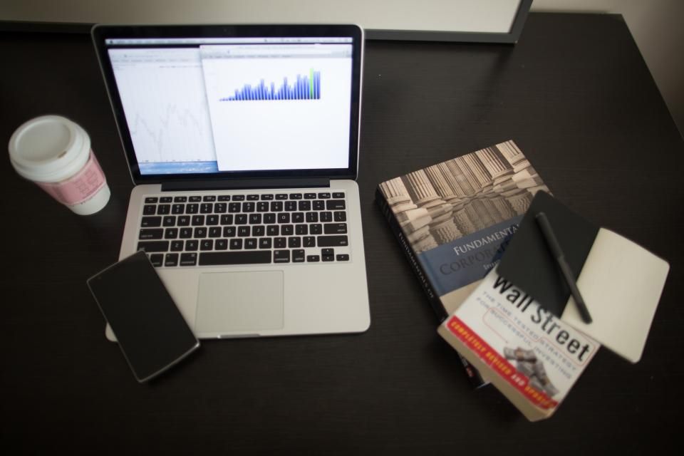 Schreibtisch von oben mit Laptop und Diagramm, Becher, Smartphone, Büchern und Notizblock, Symbolbild