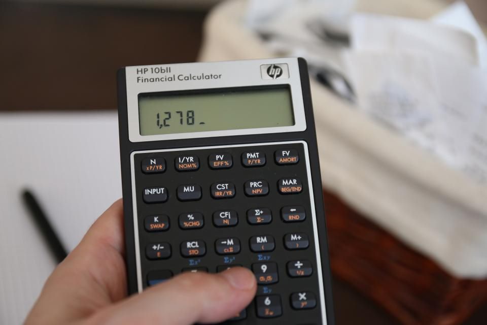 Eine Hand hält einen Taschenrechner mit Zahlenanzeige, im Hintergrund liegen Papiere, Symbolbild