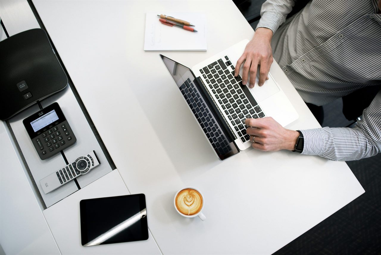 Person arbeitet von oben gesehen an einem Laptop auf einem weißen Schreibtisch